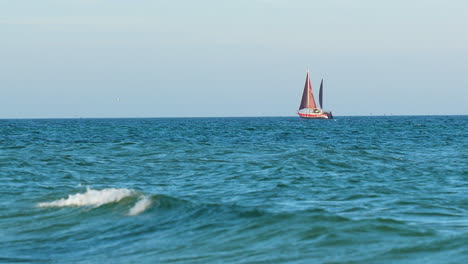 a single sailboat with red sails afloat on a calm blue sea under clear skies