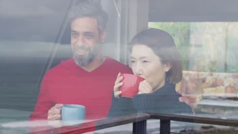 Happy-diverse-couple-drinking-coffee-and-talking-together-at-home