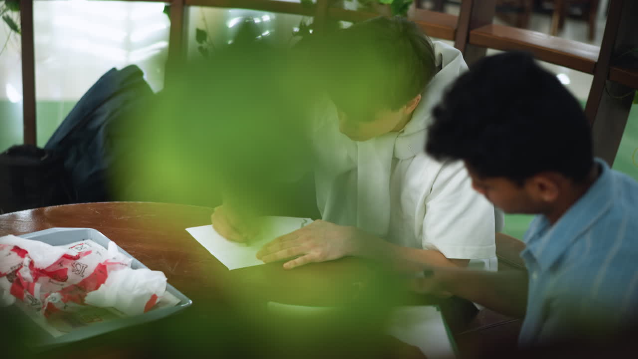 Camera focuses on pencil sketch on crisp white paper partially obscured by floral garland framing drawing area casting soft shadows adding depth to creative workspace scene under soft studio lights