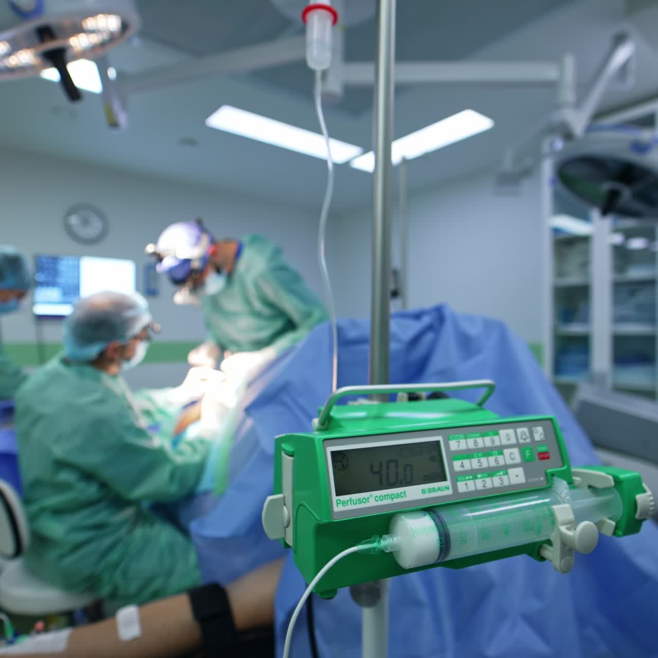 Geräte für allmähliche intravenöse Injektionen von Medikamenten am Tropfenzählerständer. Ärzteteam führt im Hintergrund eine Neurochirurgie durch