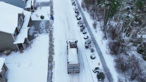 Disparo-De-Un-Dron-Siguiendo-A-Un-Camión-Volquete-Mientras-Conduce-Por-Calles-Llenas-De-Nieve-Para-Recoger-Basura