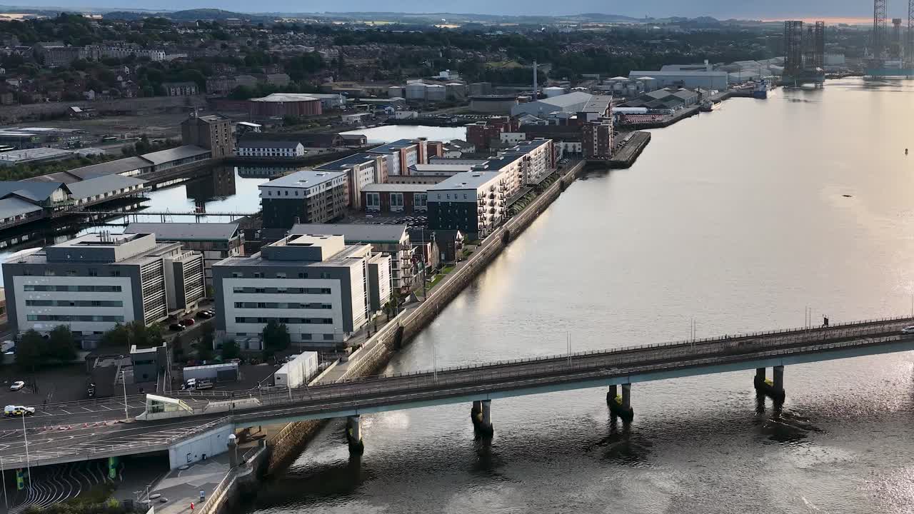 Drone camera glides over Dundee’s urban riverfront, Tay Bridge, and waterfront architecture in golden evening light