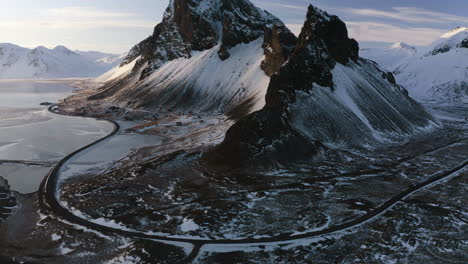 Drohnenaufnahme,-Die-Sich-über-Eine-Küstenstraße-Und-Hoch-Aufragende-Gipfel-Neigt,-Sonniger-Winterabend-In-Island