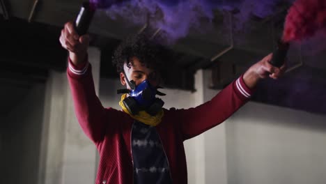 Mixed-race-man-holding-blue-and-purple-flares-standing-in-an-empty-building