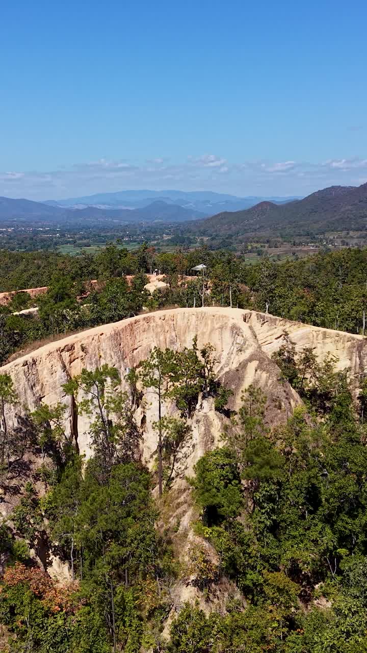 Vista aerea con drone dei sentieri scoscesi del Canyon di Pai nel Nord della Thailandia, caratterizzato da strette creste di arenaria rossa, vegetazione lussureggiante, montagne distanti all'orizzonte e un cielo azzurro limpido sopra il paesaggio mozzafiato.