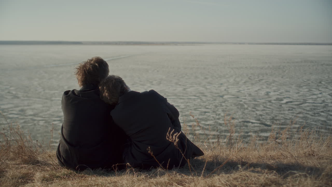 Rear View of Romantic Couple Sitting on Shore of Frozen Lake