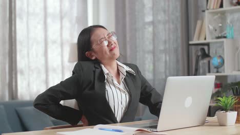 woman experiencing back pain while working on laptop at home.
