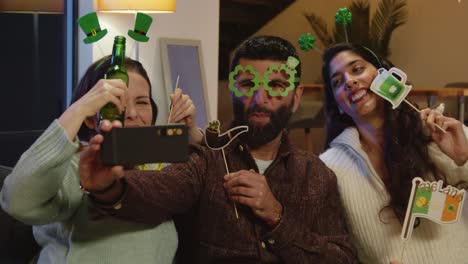 group of friends dressing up with irish novelties and props at home or in bar posing for selfie celebrating at st patrick's day party 1