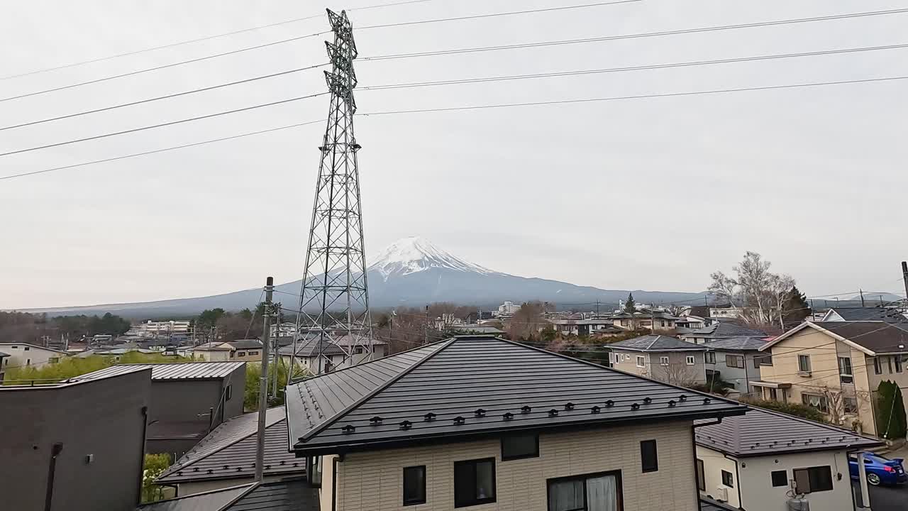 A serene view of Mount Fuji from Kawaguchiko, Japan, captured over rooftops with a transmission tower in the foreground