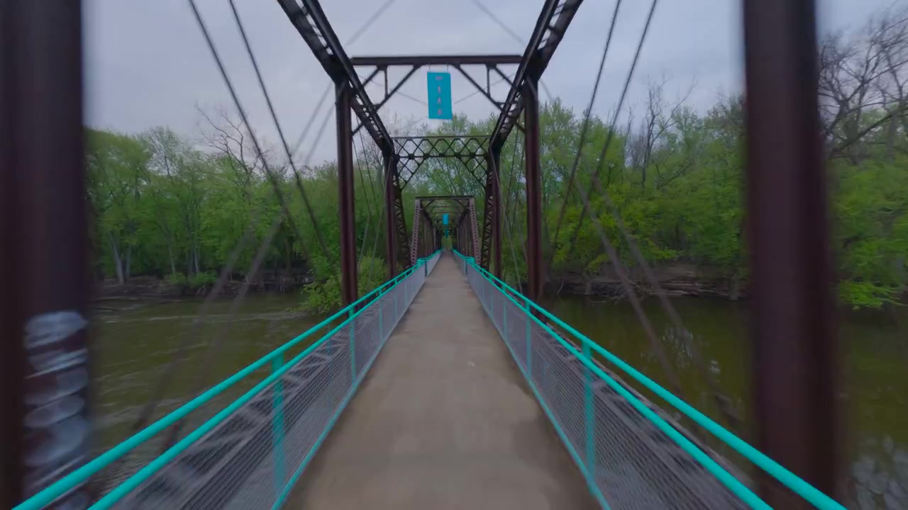 Fpv drone shot moving quickly forward on a path and crossing an old metal bridge over a river