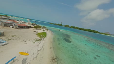 drone fpv volando rápidamente sobre una playa blanca en un pueblo de pescadores en los rocas, venezuela