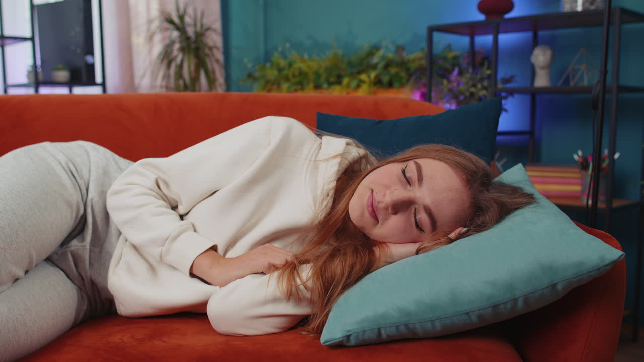 피곤한 젊은 여성이 침대에 누워 집에서 휴식을 취하고, 낮잠을 자고, 오렌지색 소파에서 잠들고 있습니다.