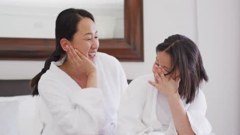 video of happy asian mother and daughter in robes having fun