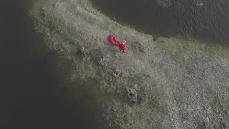 Aerial-bird's-eye-view-of-a-model-walking-on-a-tiny-island-with-bright-red-dress