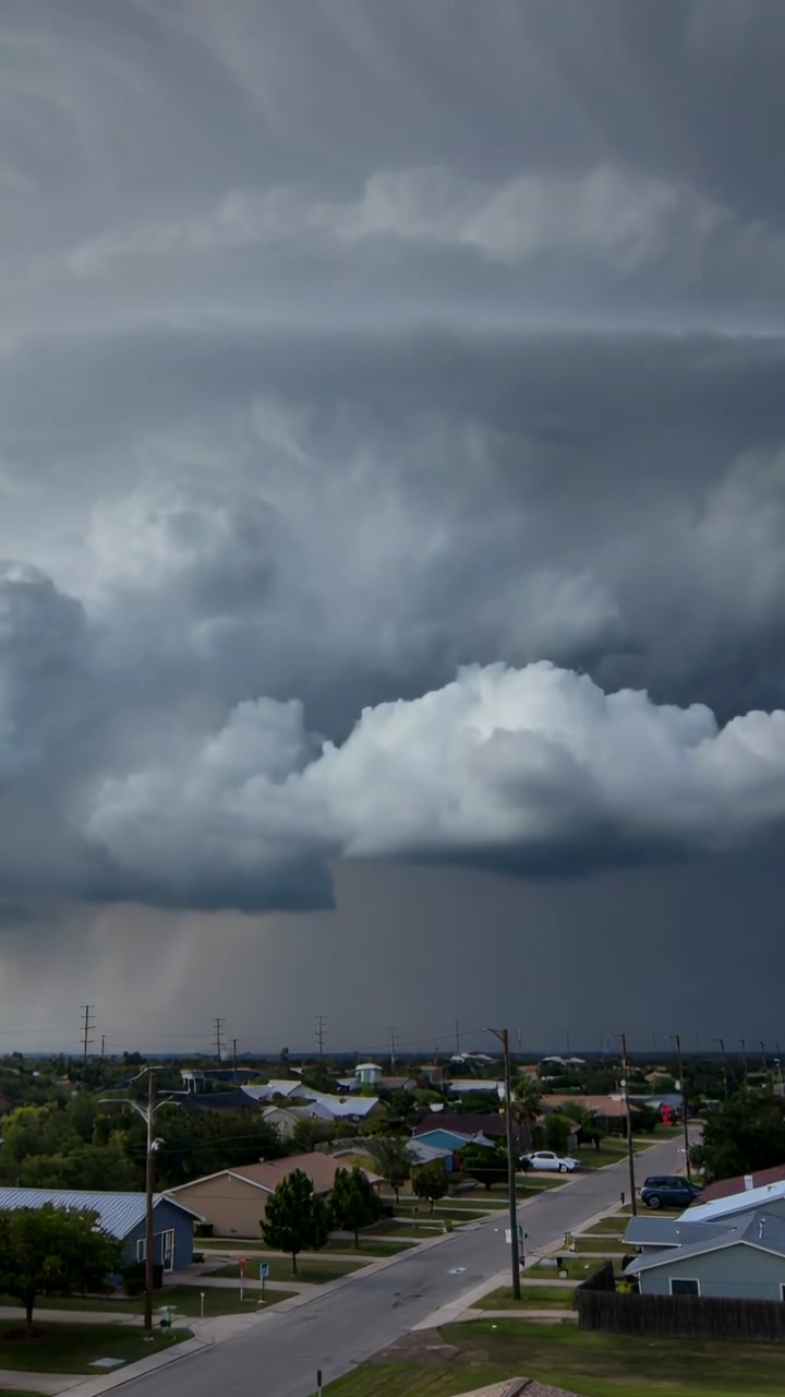 Vertical video: Approaching storm cloud lowering base over suburb, showing rain shaft and rooftops