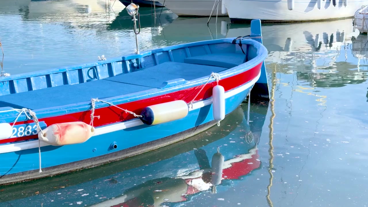 Una vivace barca di legno blu galleggia su acqua calma in un soleggiato villaggio portuale mediterraneo.