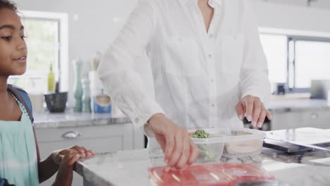 Happy-african-american-mother-and-daughter-packing-lunch-for-school-in-kitchen,-slow-motion