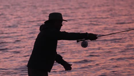 slow motion is employed to show a medium shot of a fly fisherman in silhouette at sunset in molokai, hawaii