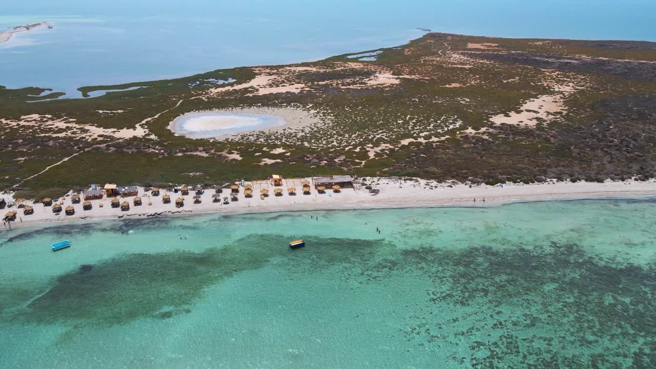 The beach is lined with several yellow umbrellas for shade, and the water appears to be crystal blue.