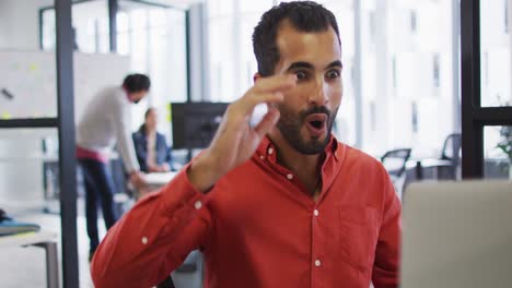 Happy-mixed-race-businessman-sitting-at-desk-using-laptop