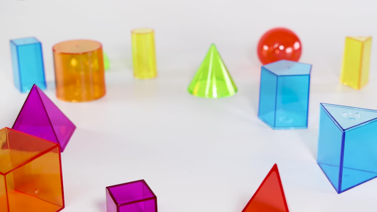 A hand arranges translucent plastic geometric shapes on a white background under bright studio lighting