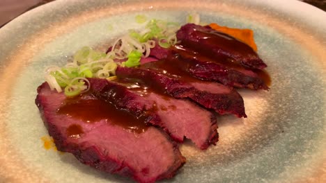 Tasty-steak-cut-in-thin-slices-with-spring-onion-and-glazed-sauce,-food-on-a-plate,-4K-shot