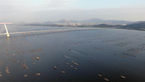 Hong-Kong-Shenzhen-Bay-Bridge-with-Tin-Shui-Wai-buildings-in-the-horizon-and-Fish-and-Oyster-cultivation-pools,-Aerial-view