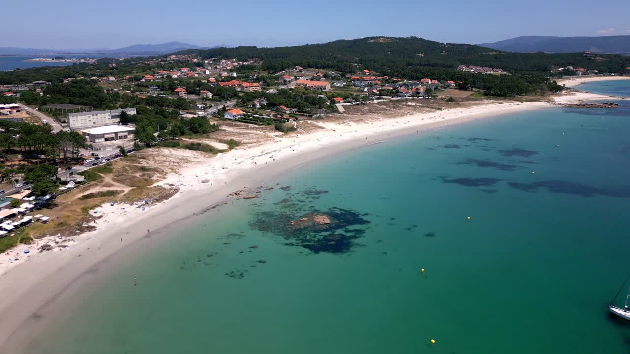 Ripresa aerea di un villaggio sulla spiaggia e di un mare cristallino color giada a Sanxenxo, Spagna