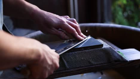 hands meticulously sharpening a knife on a whetstone