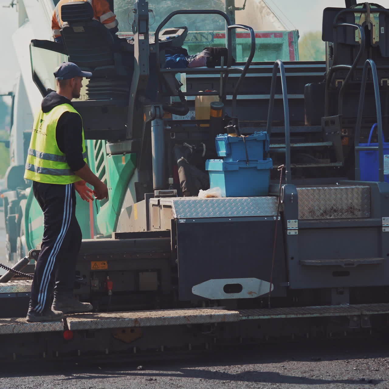 Asphalt paver and workers on the road. Fresh asphalt resurfacing the street. Workers in a huge machinery for making a new road. Roadworks outdoors.
