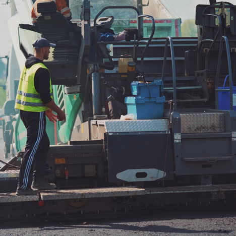 asphalt paver and workers on the road. fresh asphalt resurfacing the street. workers in a huge machinery for making a new road. roadworks outdoors.