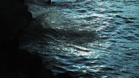 moody waves crashing into dark rocks at sunset in slow motion moody