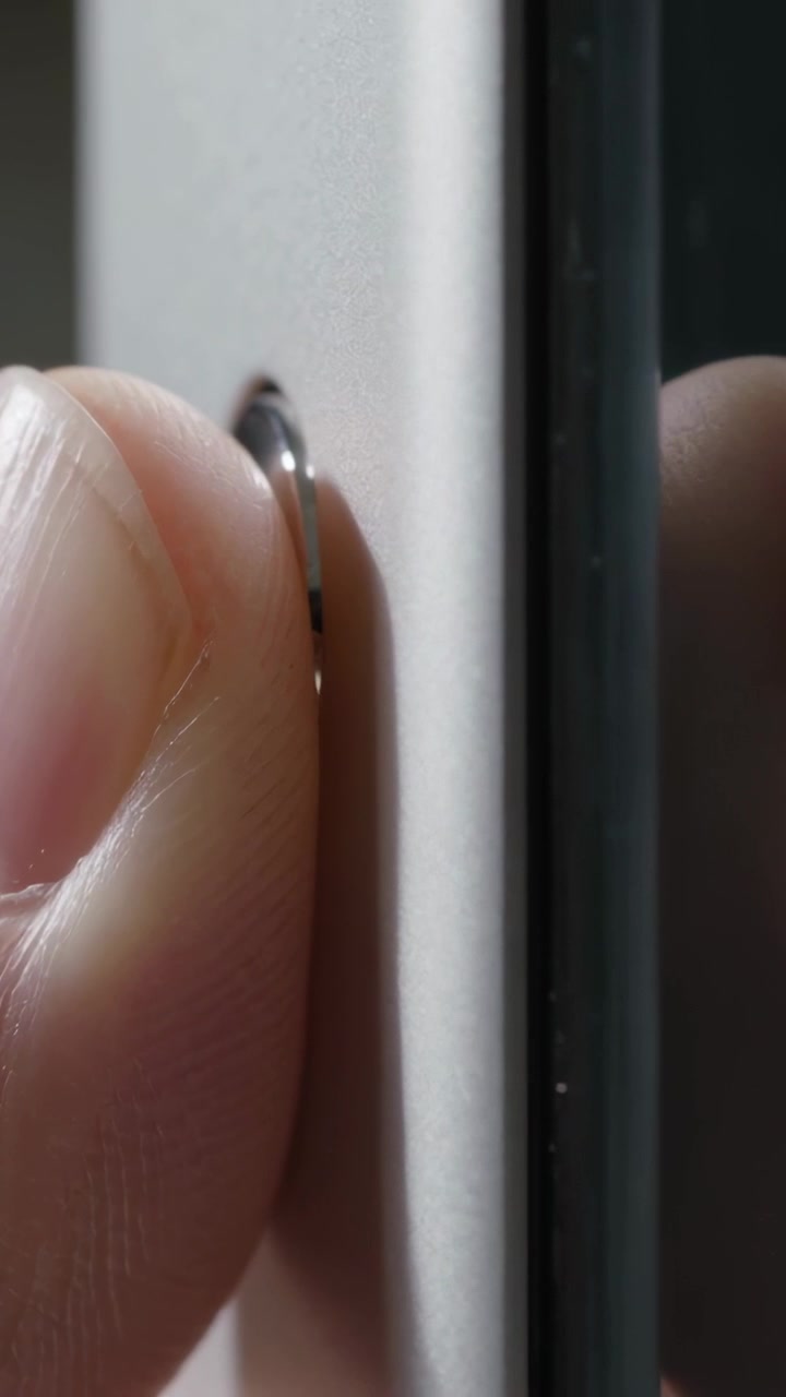 Video verticale: Pollice e indice che posizionano un disco metallico a filo su un pannello bianco vicino alla cornice.