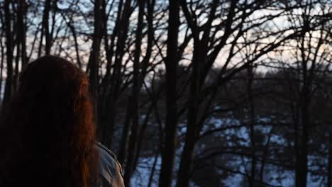 young girl with beautiful red hair illuminated by sunset's light while watching at the landscape