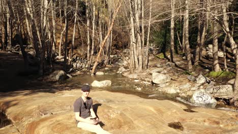 slow aerial reverse dolly tilt of a young white male hiker sitting on top of etiwanda falls in rancho cucamonga california raging waterfall