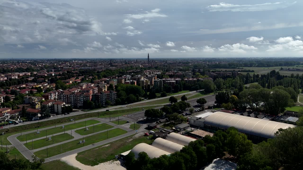 Luftfoto af Cremonas bybillede, der møder landskabet i Lombardiet, Norditalien, med Torrazzo klokketårn i baggrunden og sportsfaciliteter i forgrunden