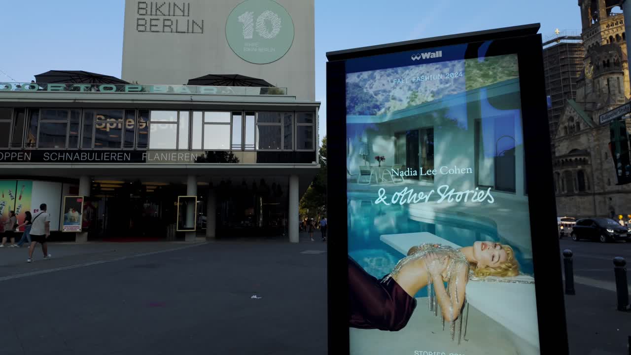 Vibrant street in Berlin during the IFA event, featuring Bikini Berlin and an illuminated billboard. The camera tilts up to capture the architecture and urban atmosphere in a dynamic city setting