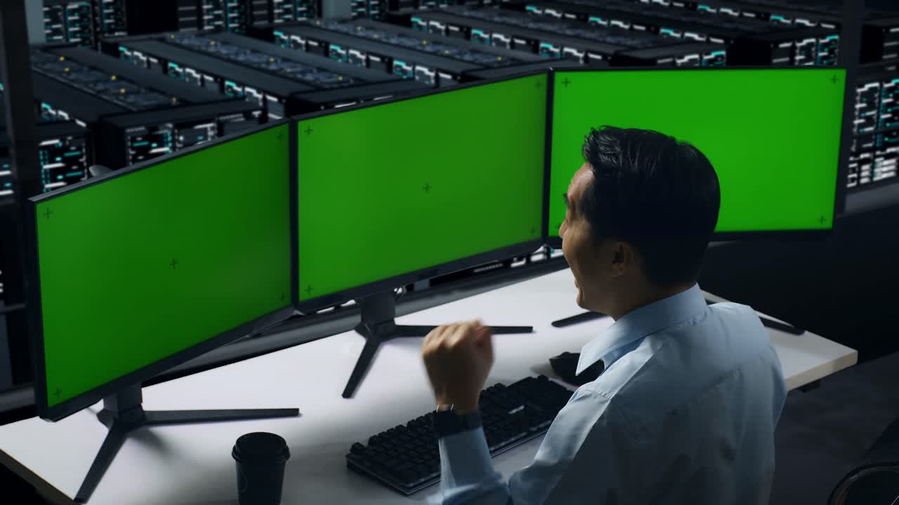 Vista posteriore di un uomo asiatico stanco che sbadiglia mentre lavora con monitor multipli in un data center.
