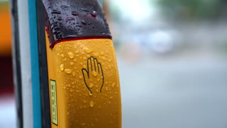 button for traffic light at the crossroads with blurred car in background during a raining da