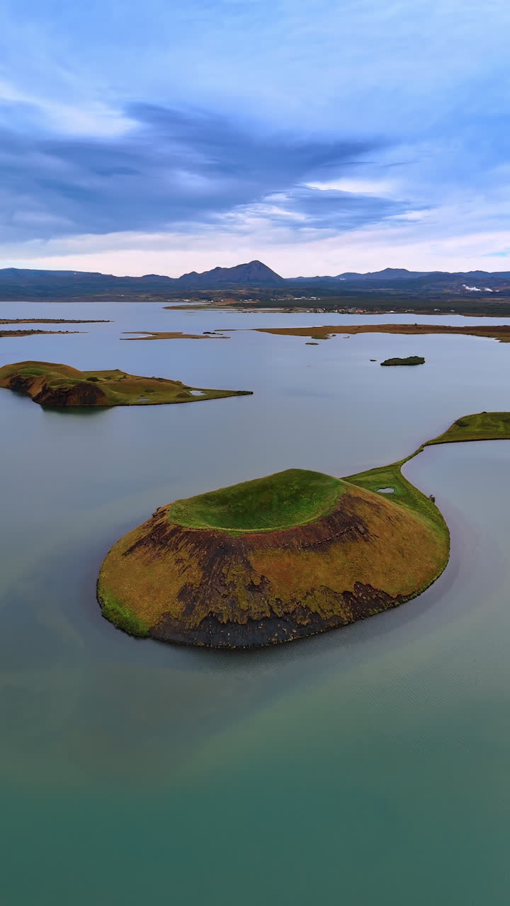 Little islands of diverse shapes sticking out of water. Remarkable nature of Iceland. Mountain range at backdrop. Vertical video.