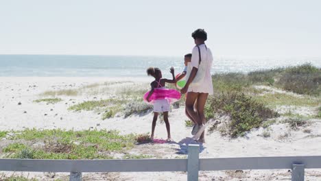 Happy-african-american-family-with-beach-equipment-walking-on-beach-in-a-sunny-day