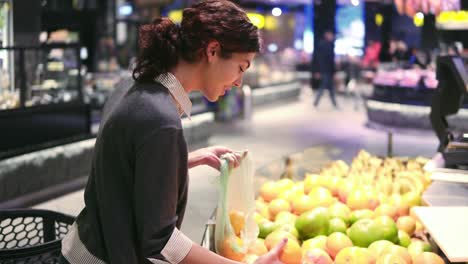 una hermosa chica morena de unos 20 años recogiendo naranjas en una bolsa de plástico en el pasillo de frutas y verduras de una tienda de comestibles.