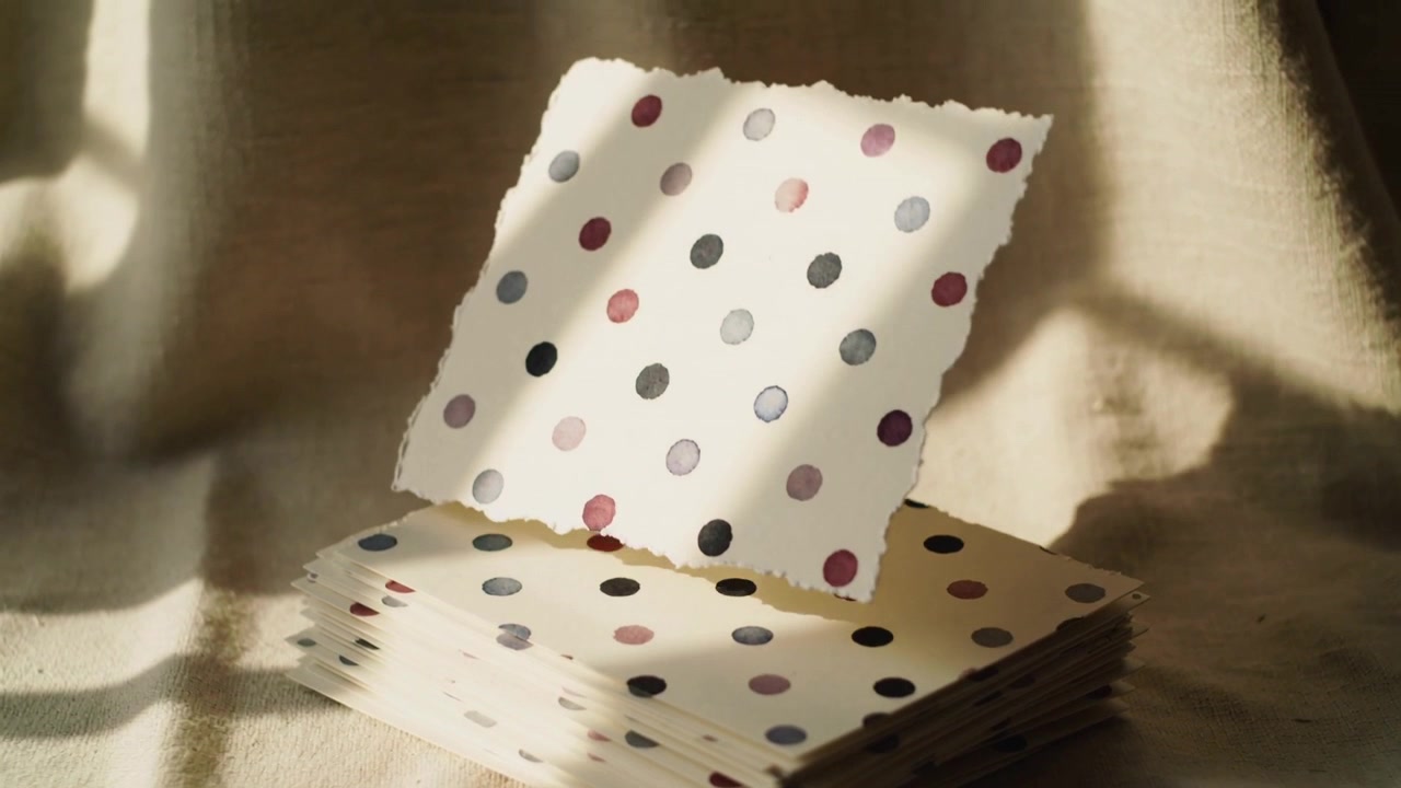 Breeze lifting top sheet from polka-dot napkin stack on cloth tabletop, sheet rotating and hovering