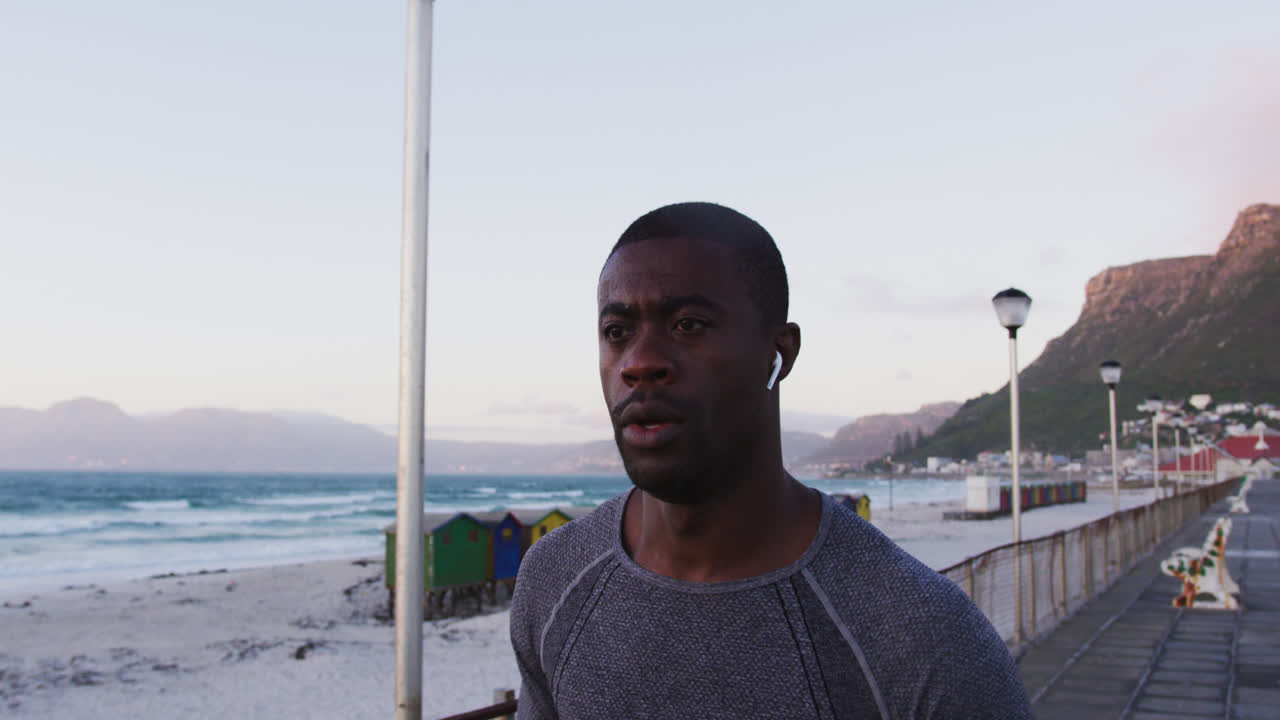 сосредоточенный афроамериканский мужчина тренируется на открытом воздухе, бегает по берегу моря с беспроводными наушниками