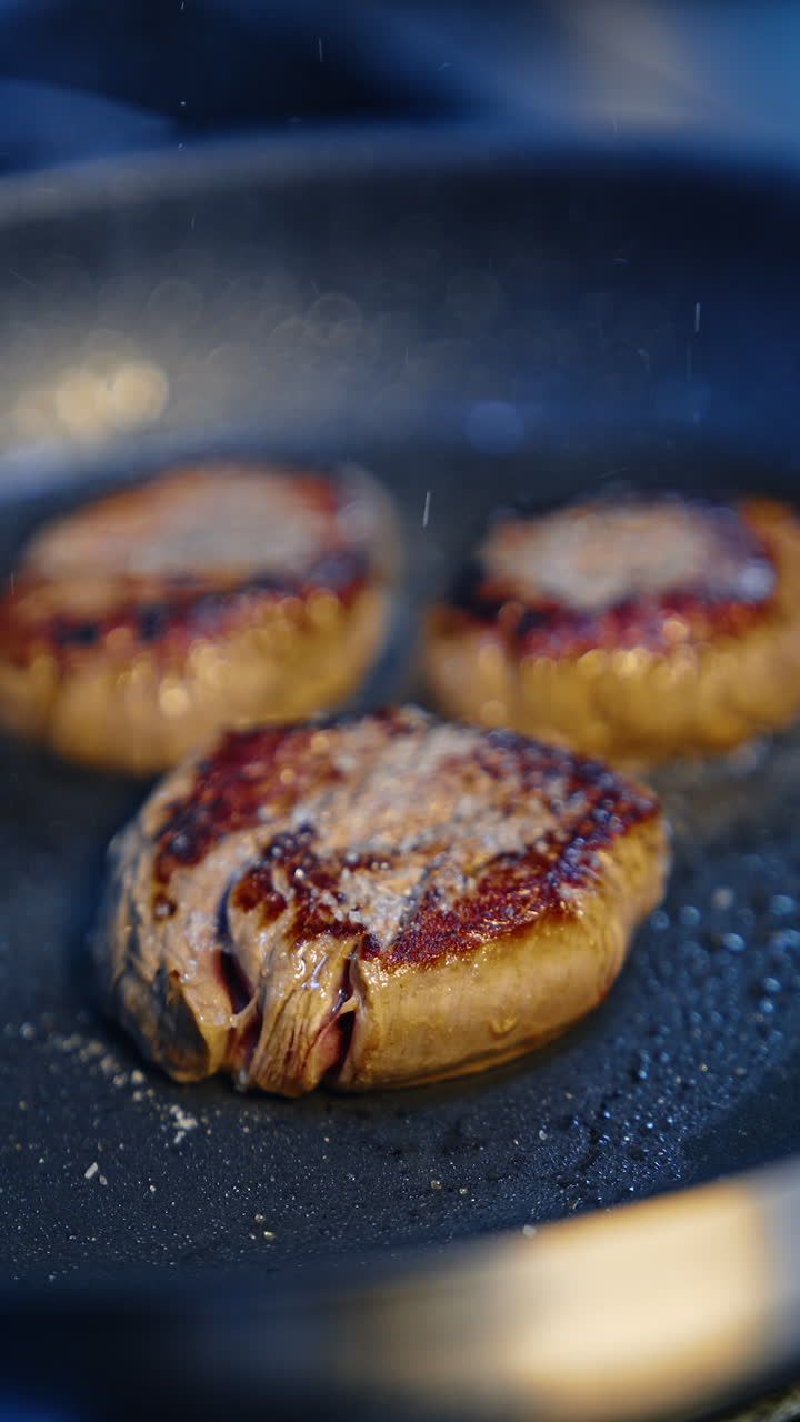 Meat chops are prepared in oil. Cook uses metal tongs to turn the beef. Close up. Vertical video.