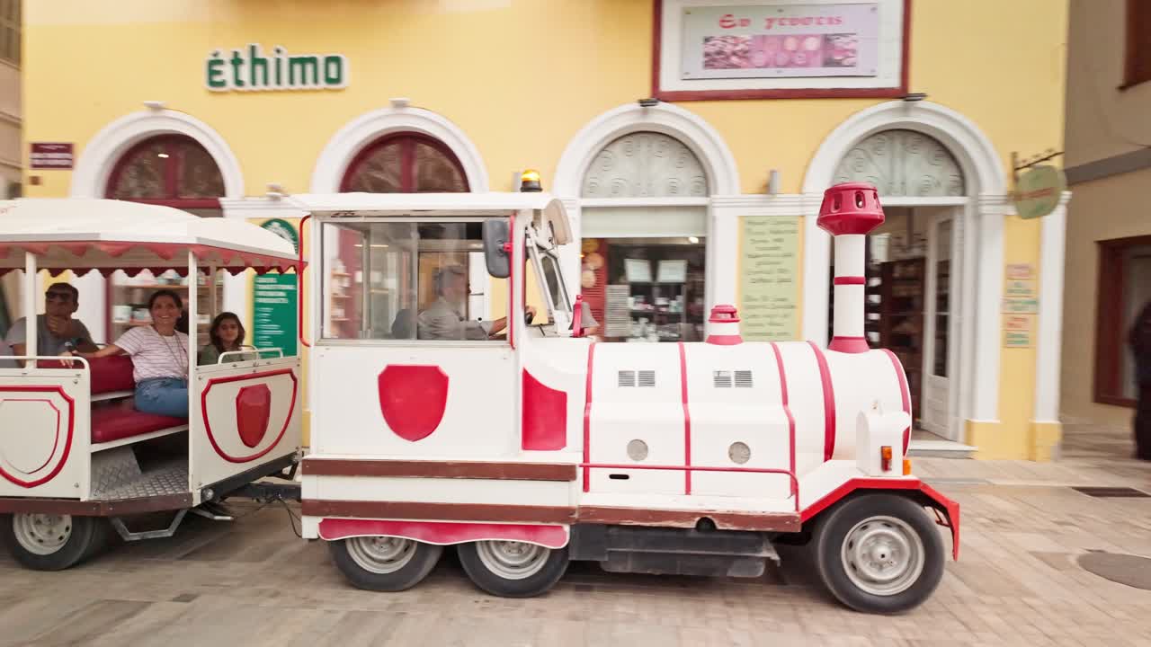 Tourists ride sightseeing road train Greek town narrow paved streets