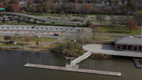 aerial-clockwise-orbit-over-Meadow-Lake-on-a-beautiful-day-with-a-brick-buliding-with-a-wooden-pier---many-seagulls-basking-in-the-sun-in-Flushing-Meadows-Corona-Park,-Queens,-NY