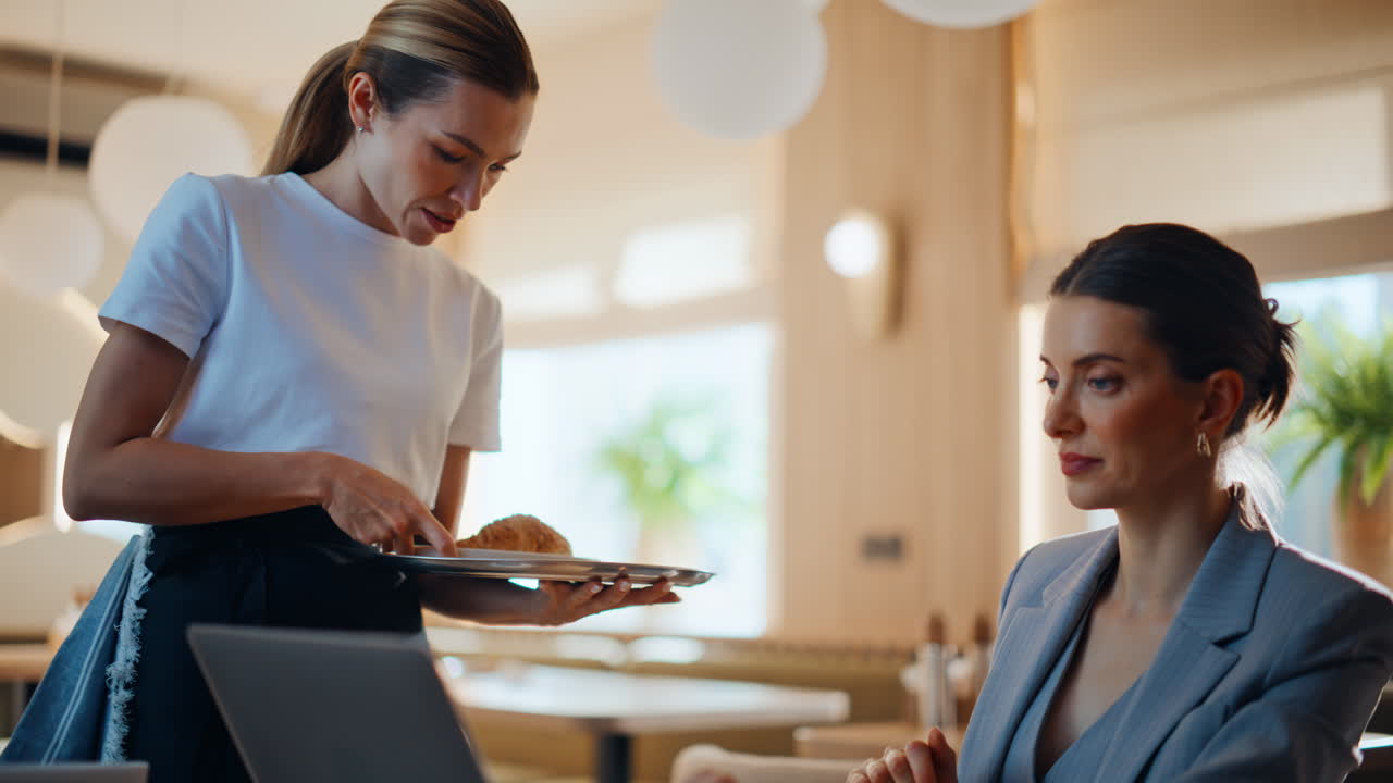 Forretningskvinne som skriver på bærbar PC i kafeteria, og koser seg mens servitøren kommer med kaffe