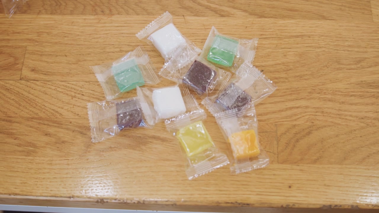 Hand removing detergent pods from wooden counter in kitchen, kitchen assistant picking packets one by one, scattered arrangement turning into isolated leftovers, closeup motion and texture with warm