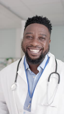 vertical video of portrait of happy african american male doctor looking at camera in slow motion